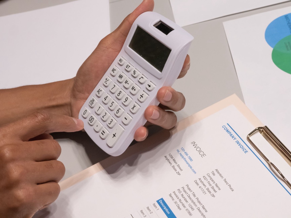 Hands using a calculator next to a company invoice, representing a cost calculation.