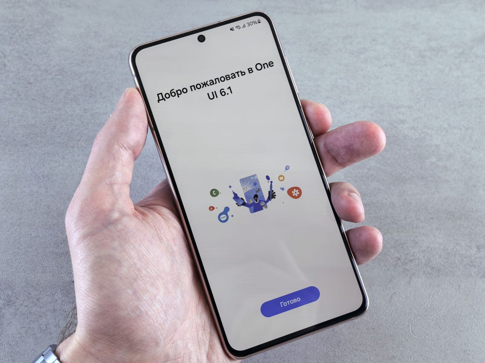 A hand holding an Android phone displaying a One UI welcome screen during setup.