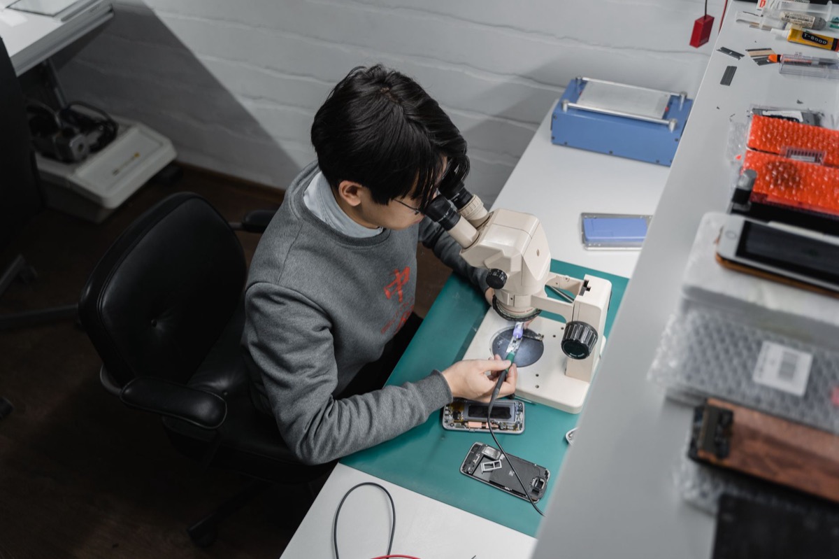 A technician inspects a smartphone under a microscope at a repair bench.
