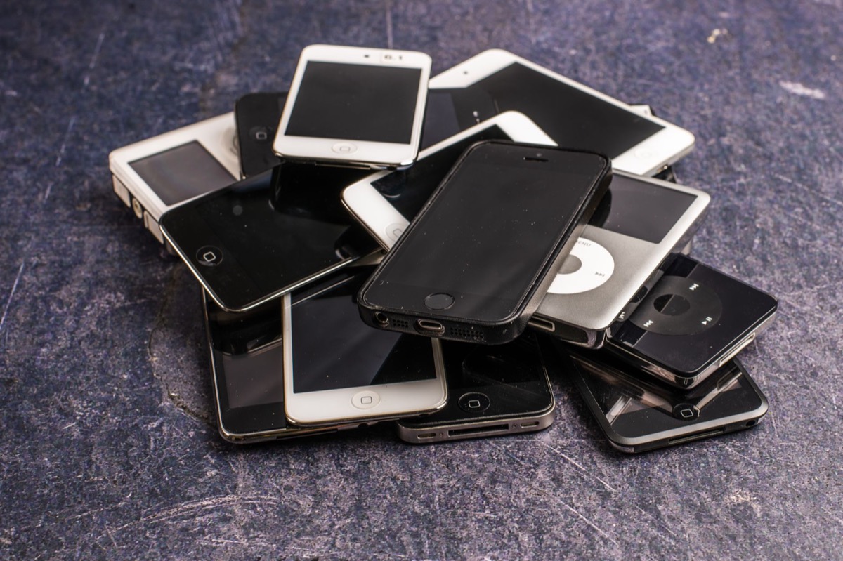 A stack of assorted used mobile phones with dark screens on a grey background.