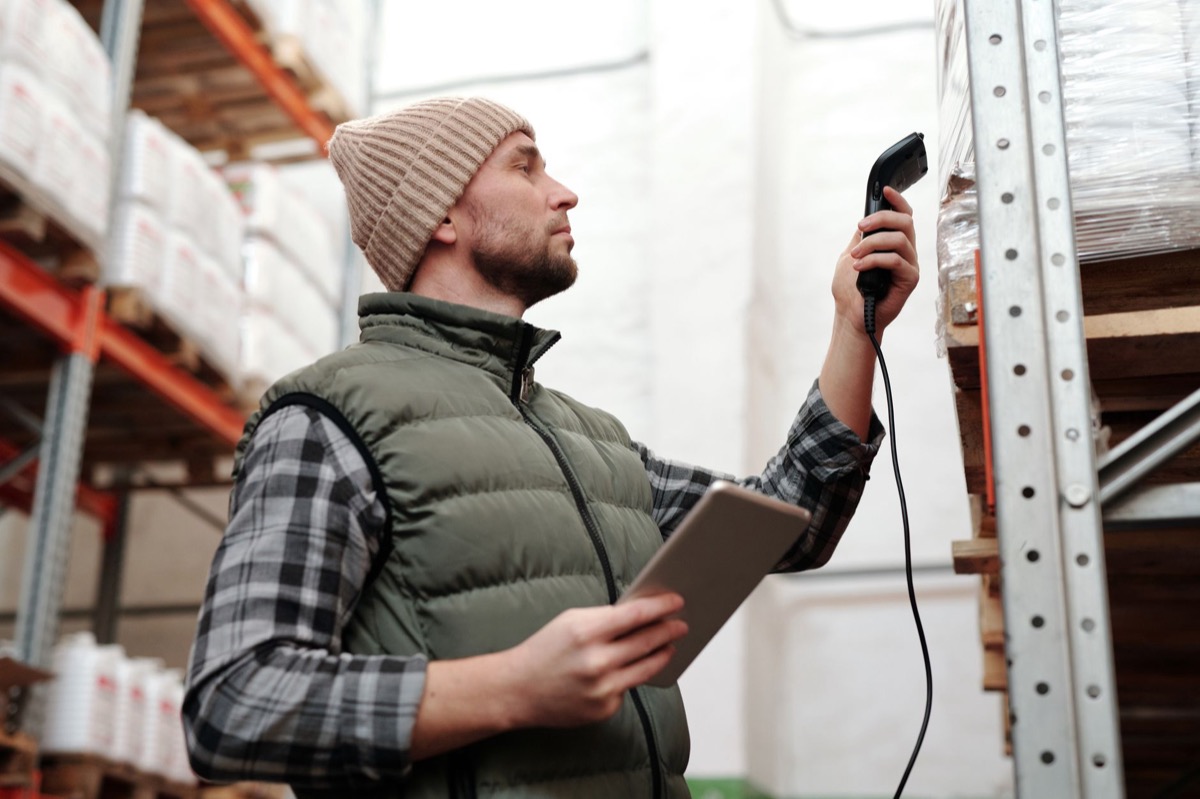 A warehouse worker scans inventory with a handheld scanner and tablet.