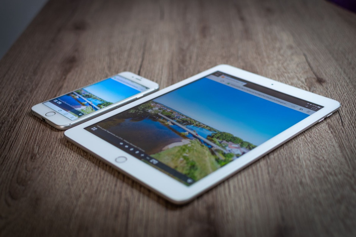 A tablet and phone showing a scenic landscape image on a wooden table.