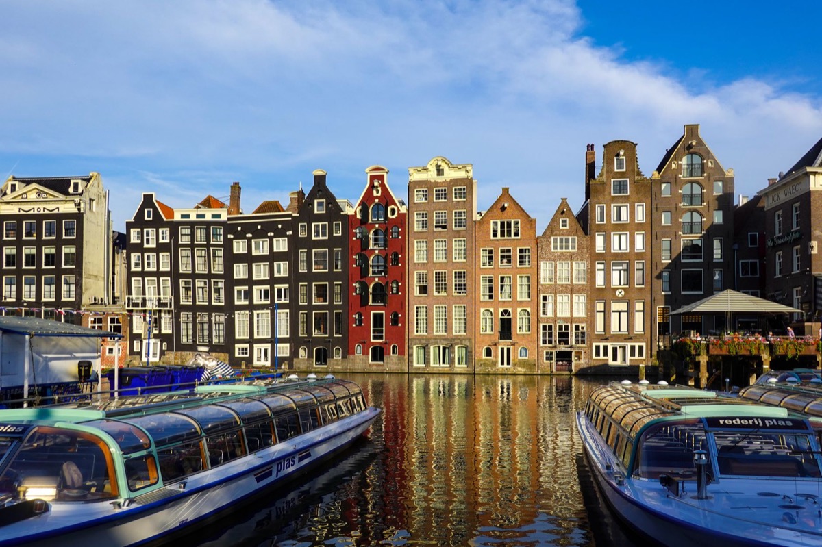 Colorful historic buildings along an Amsterdam canal with boats in the foreground.
