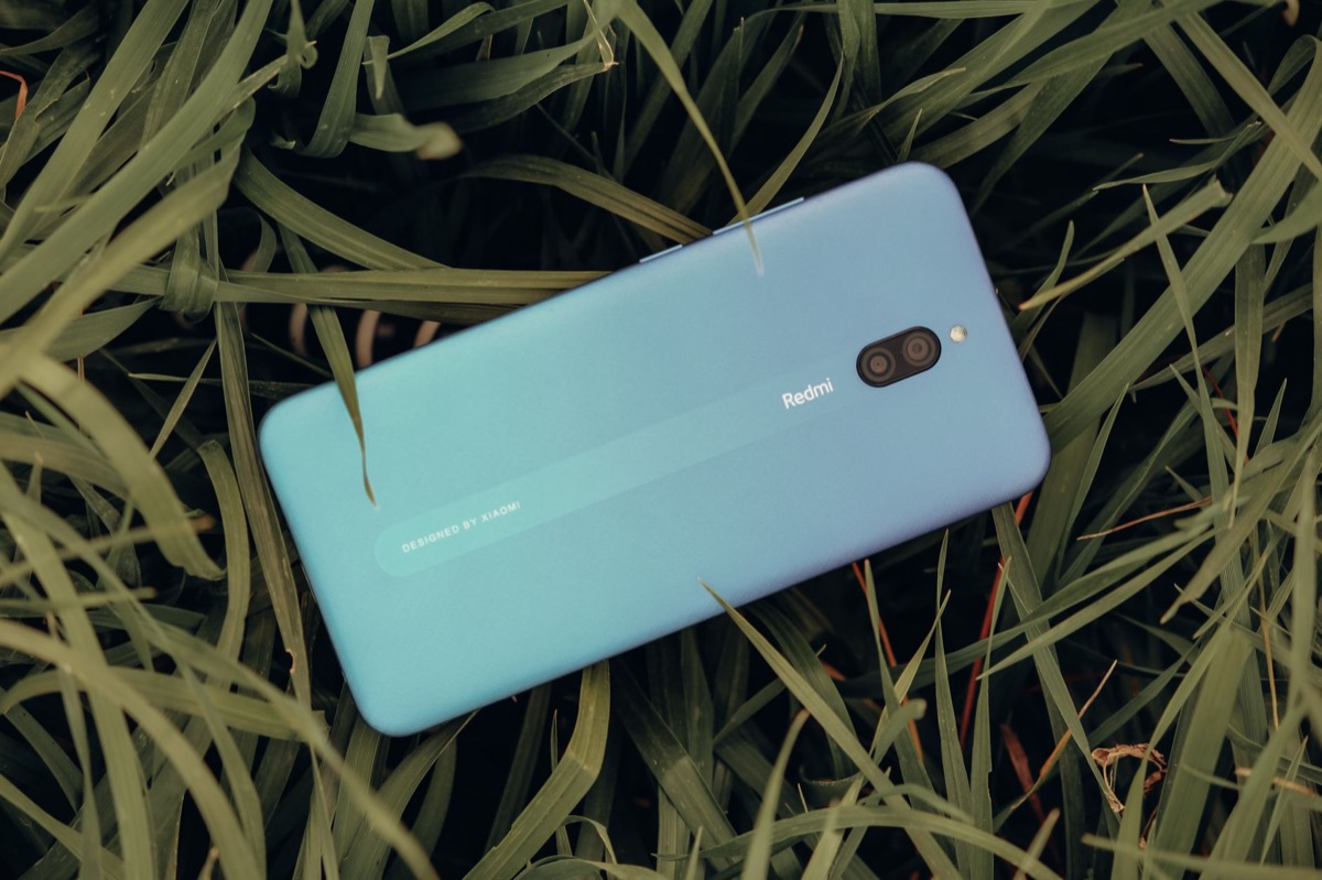 A blue smartphone resting outdoors on lush green grass.