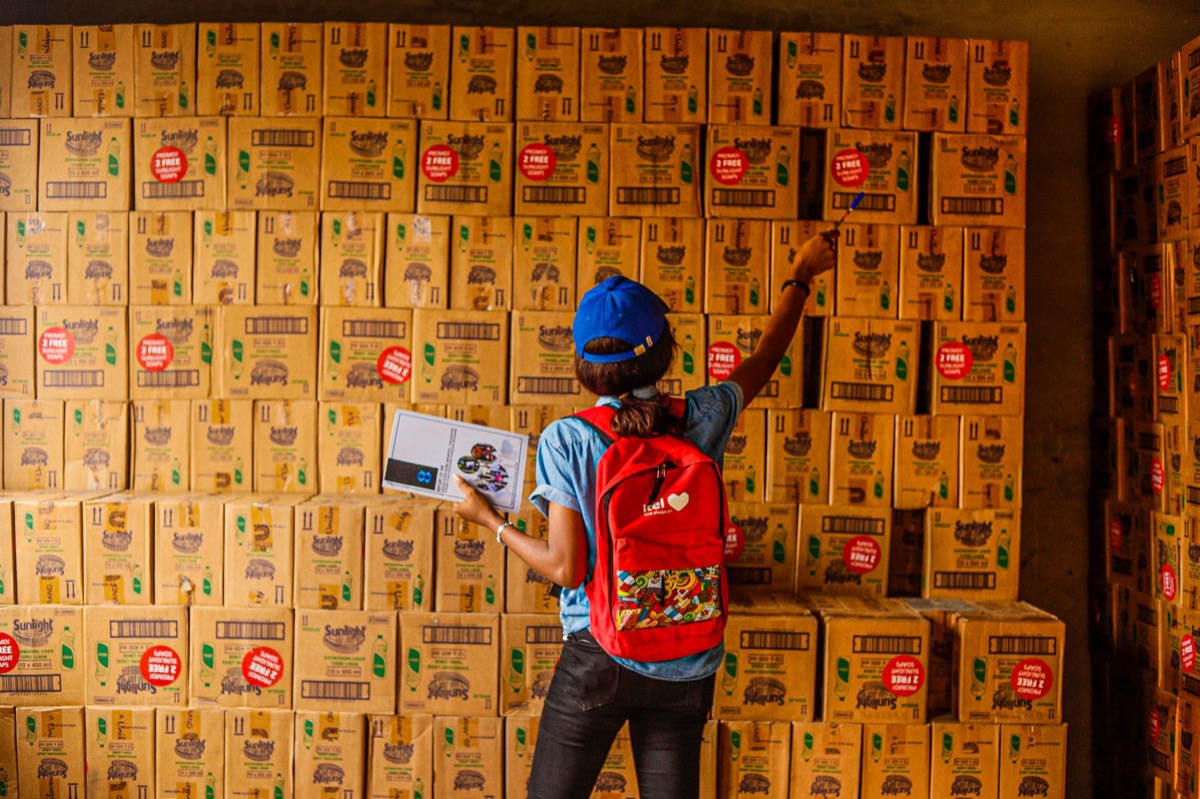 A person organizing inventory with a clipboard in a warehouse full of boxes.