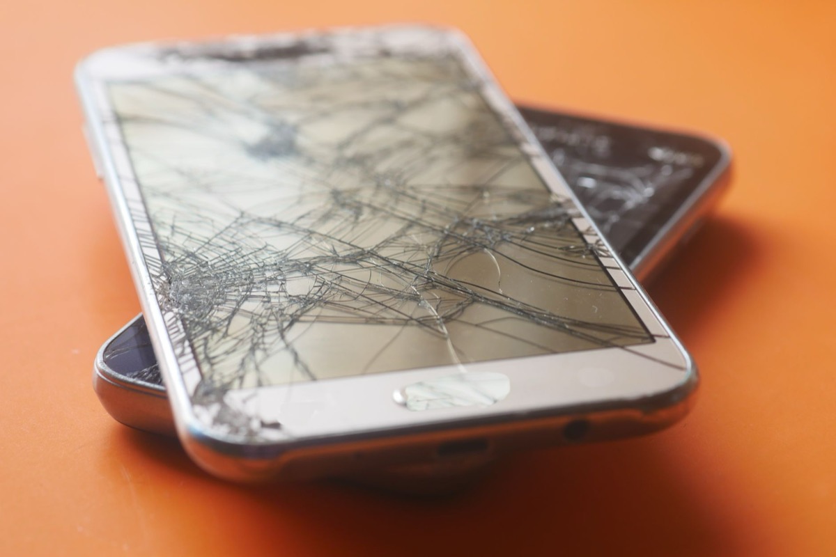 Two broken smartphone screens with cracked glass on an orange background.