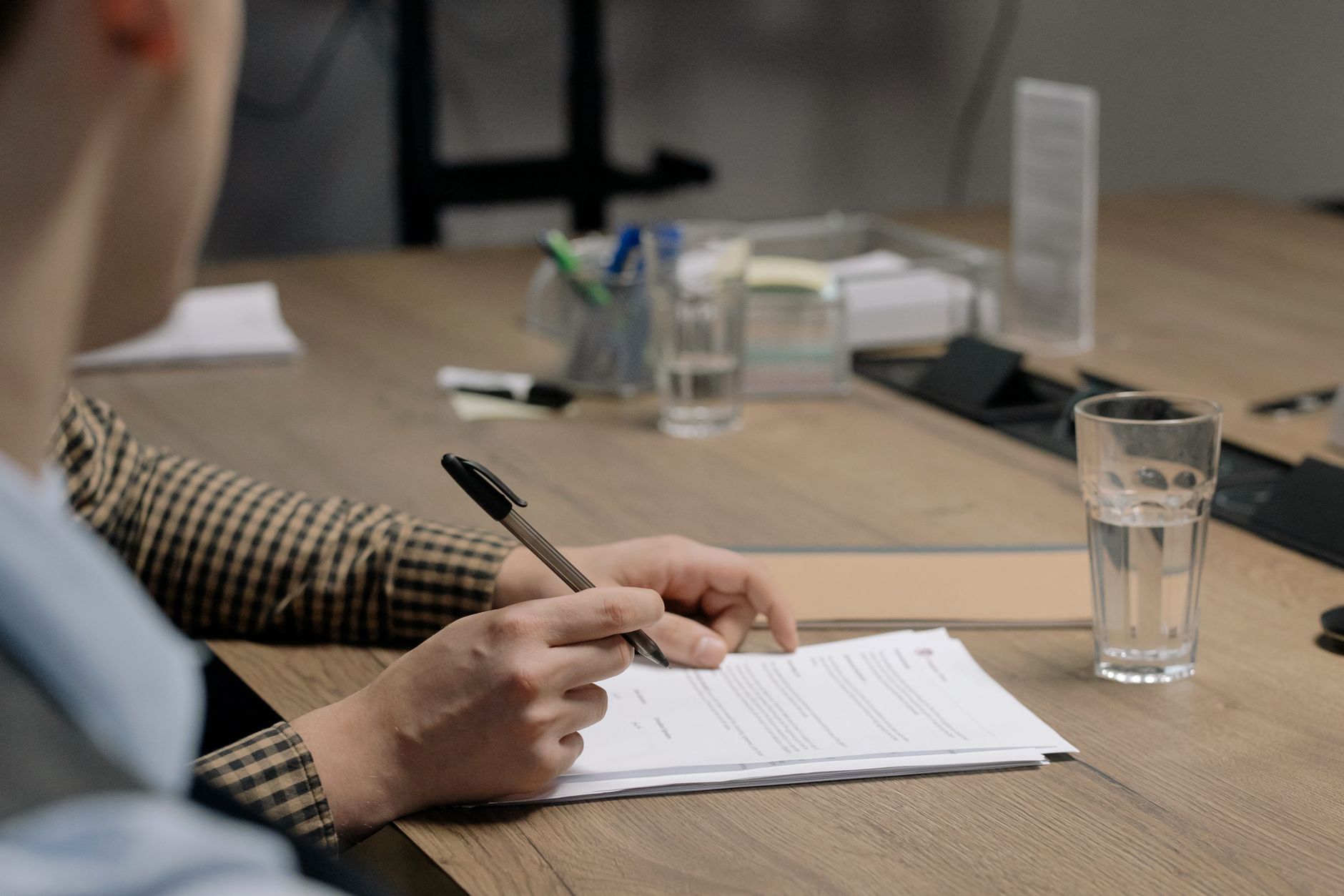 A person signing a business document at a wooden desk.