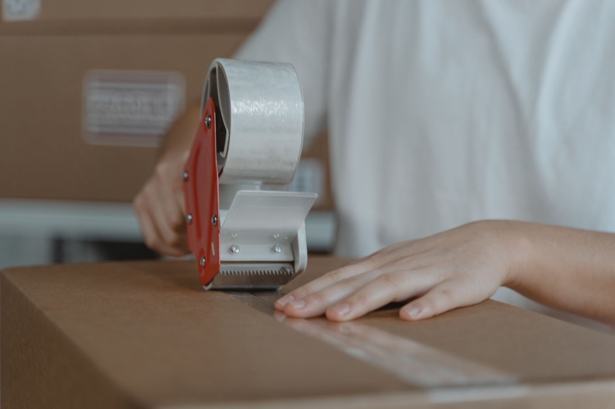 A person sealing a cardboard box with tape, packaging it for shipment.