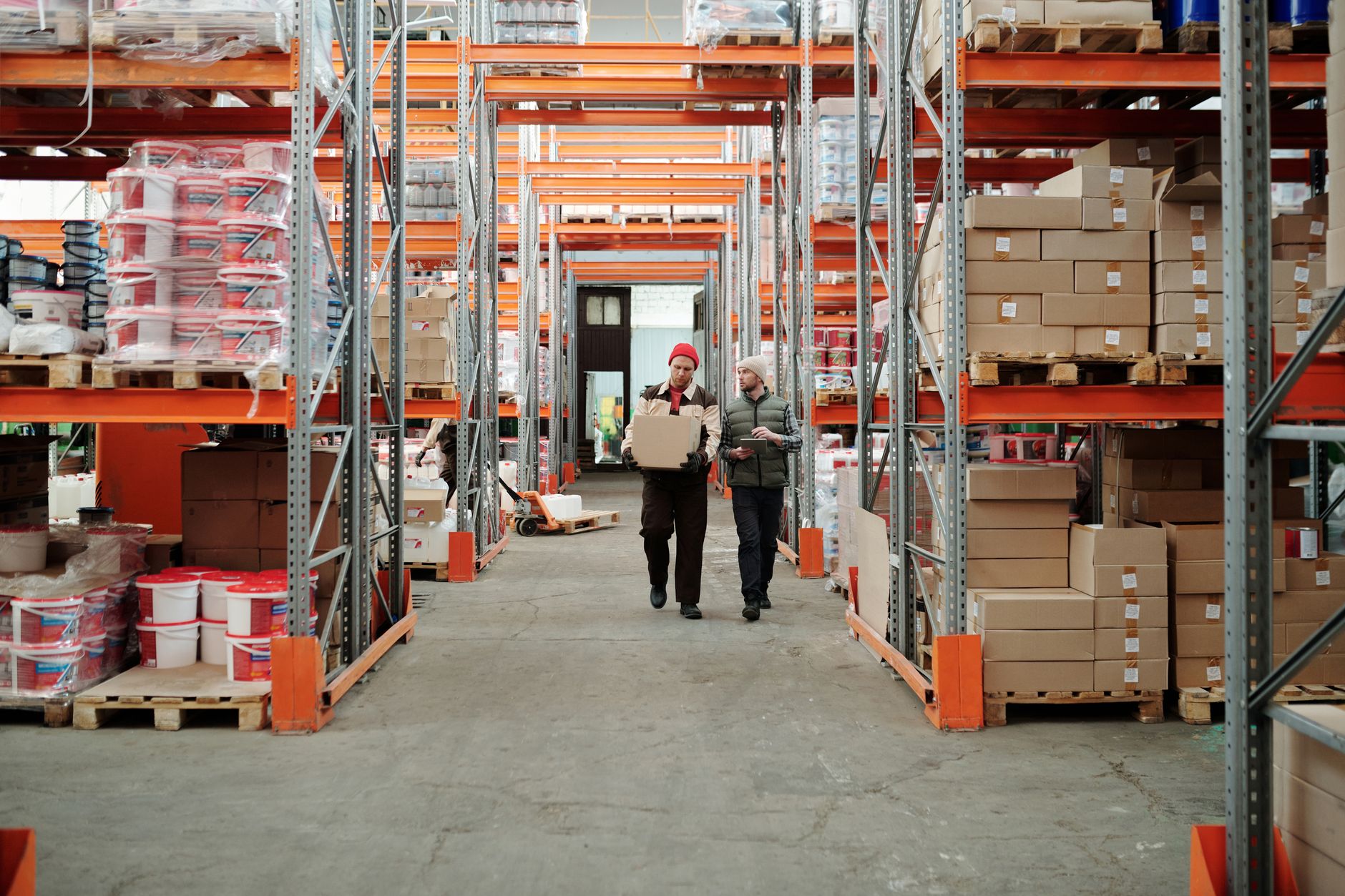 Warehouse workers handling a package among stacked goods.