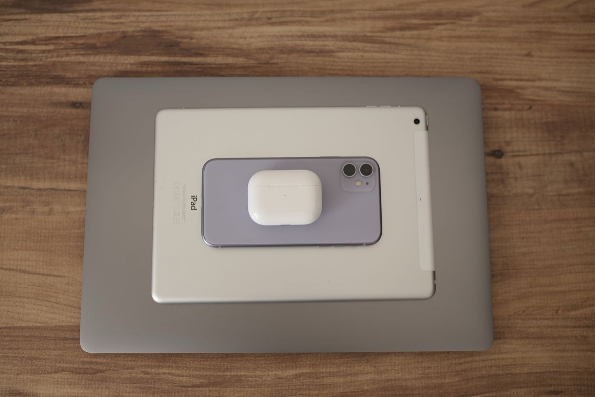 A flat lay of modern technology devices including a smartphone, tablet, and earbuds on a wooden table.