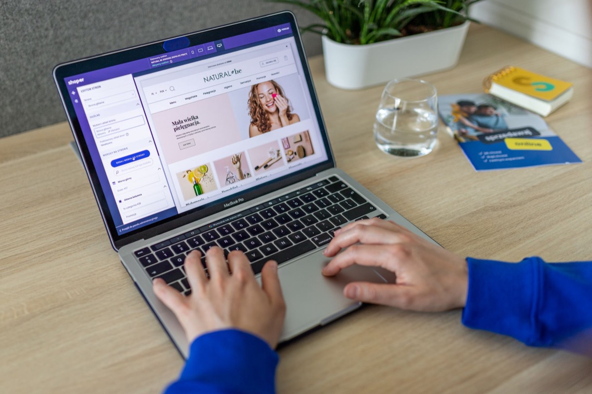Hands typing on a laptop showing an e-commerce website in a modern office.